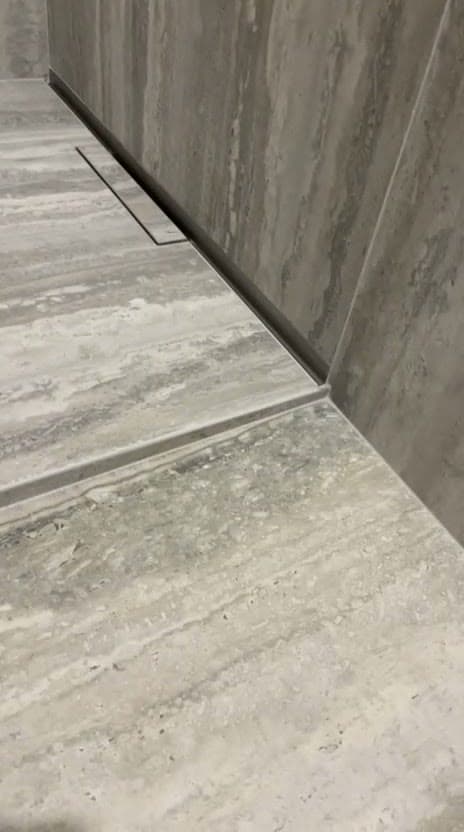 Caniveau linéaire au pied du mur d’une douche à l’italienne à Gex, coupe marquant la rupture de pente dans le grès effet travertin gris