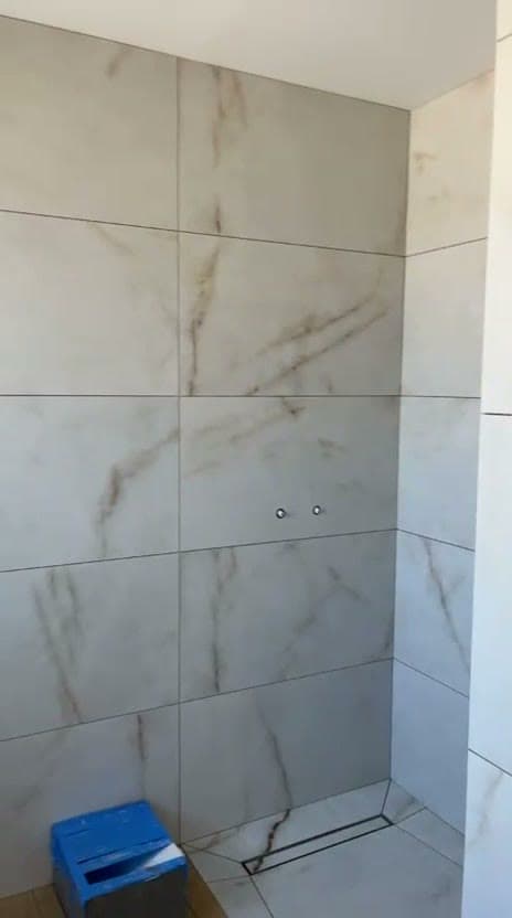 Mur de douche à l’italienne à Divonne-les-Bains en carrelage grand format effet marbre blanc posé à l’horizontale, caniveau linéaire et attentes de robinetterie