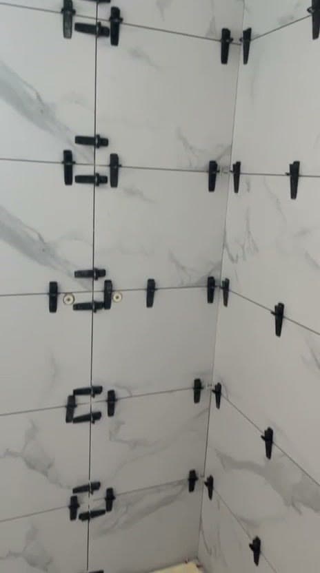 Angle de mur en faïence grand format effet marbre blanc veiné gris, clips noirs de nivellement aux joints, pendant la pose à Saint-Genis-Pouilly