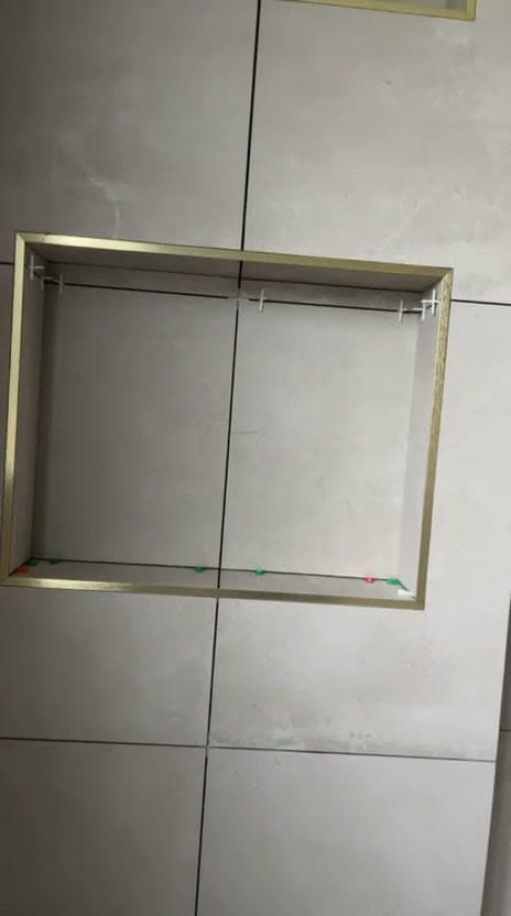 Niche murale bordée de profilés dorés en cours de pose dans un carrelage beige grand format, croisillons encore en place, à La Motte-Servolex
