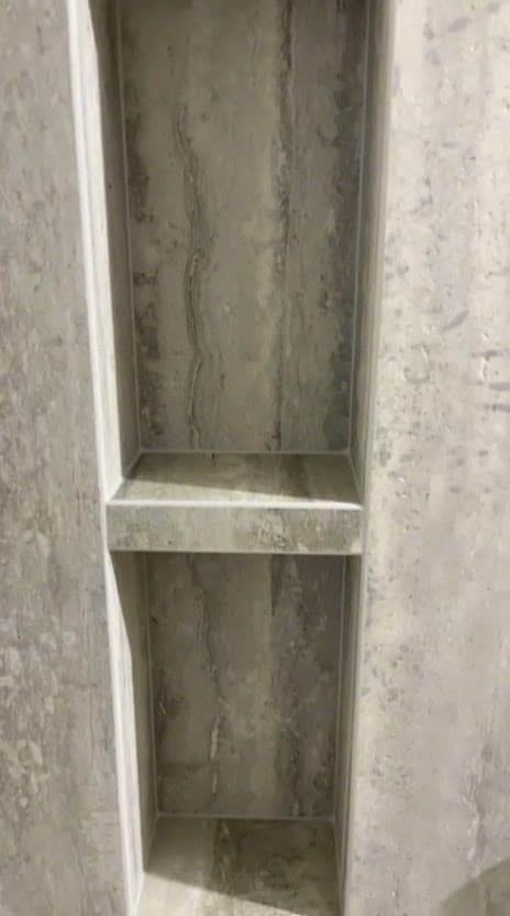 Niche murale à deux compartiments dans une douche à Gex, tablettes et retours taillés dans le même grès effet travertin gris