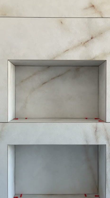 Deux niches superposées habillées de grès effet marbre blanc veiné beige, arêtes nettes sans profilé, cales encore en place, à Divonne-les-Bains
