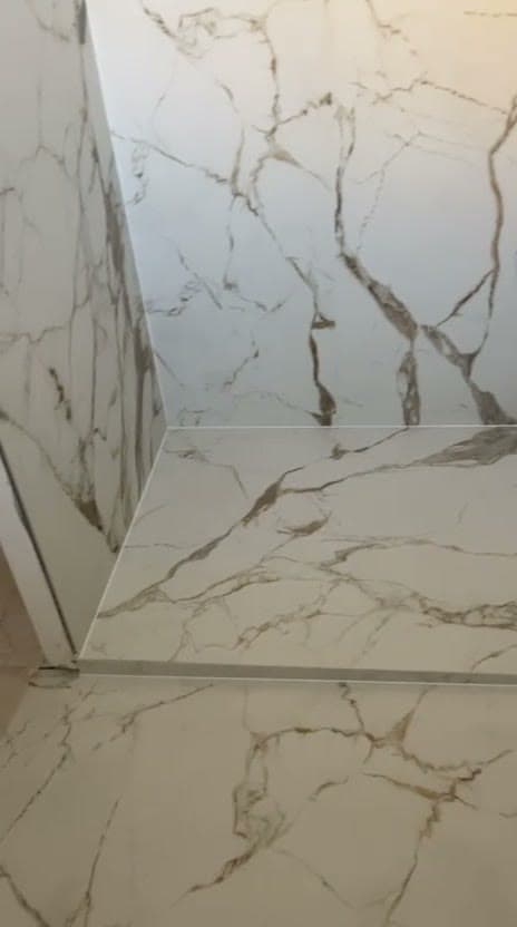 Angle de douche à Divonne-les-Bains en grès très grand format effet marbre blanc veiné doré, rebord carrelé habillé du même matériau