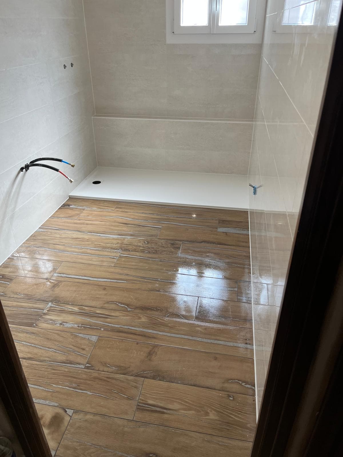 Sol en grès cérame imitation parquet posé à joints décalés, encore humide et en cours de nettoyage, devant un receveur extraplat à Albertville