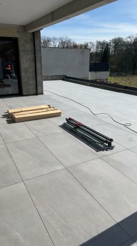 Terrasse en partie couverte à Saint-Julien-en-Genevois, dalles de grès cérame gris effet pierre à joints fins, coupe-carreau encore sur place