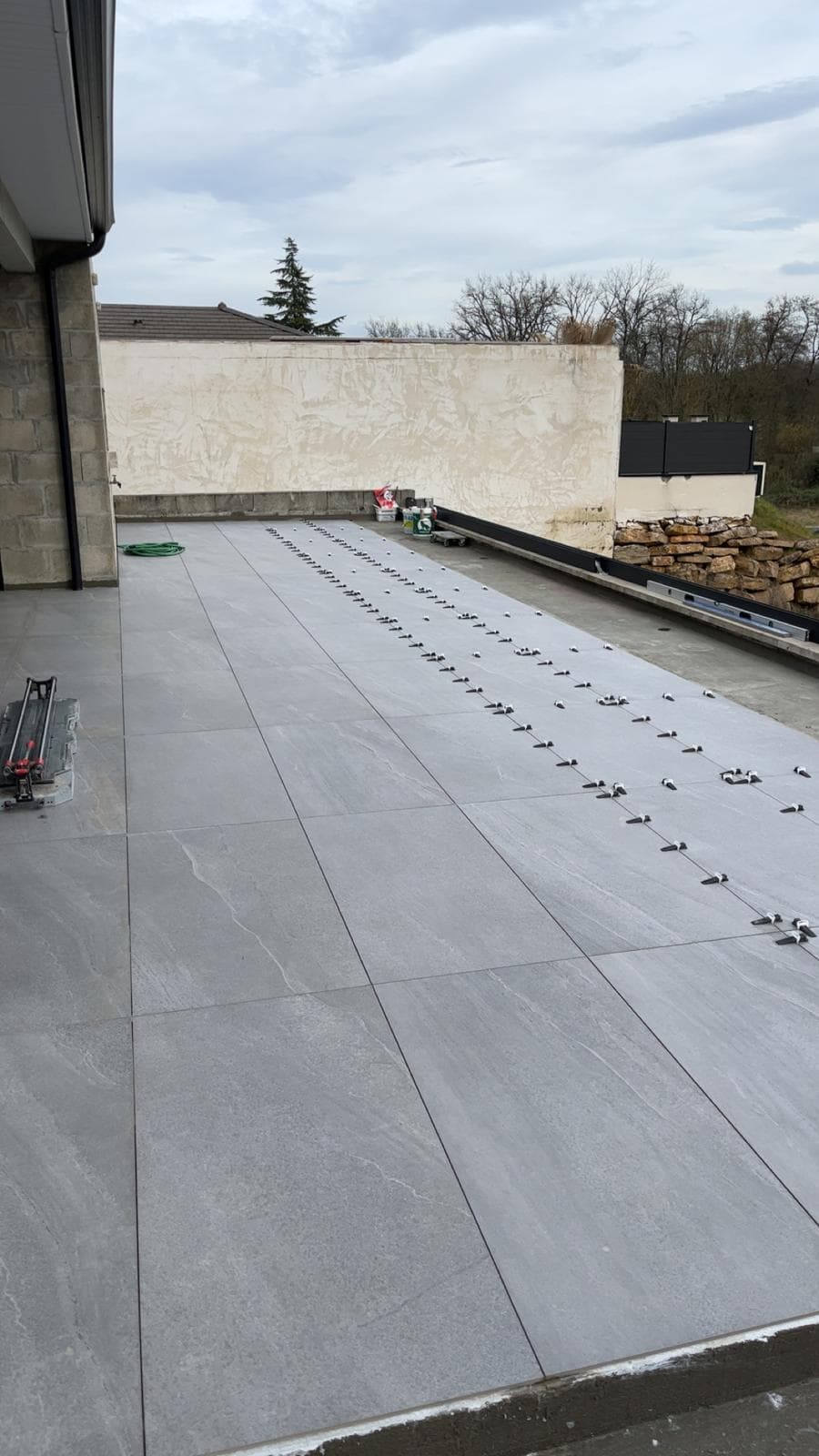 Pose de dalles de terrasse en grès cérame gris grand format à Saint-Julien-en-Genevois, clips et cales de nivellement sur les derniers rangs, coupe-carreau manuel