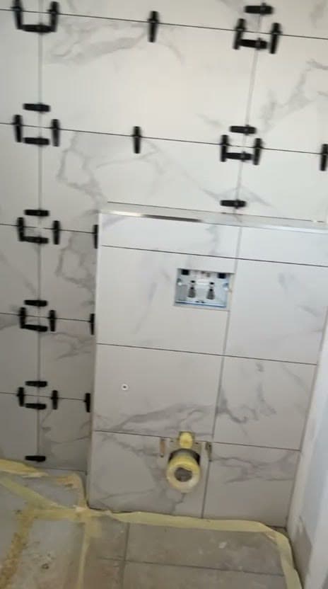 Coffrage de WC suspendu habillé de carrelage effet marbre blanc à Saint-Genis-Pouilly, réservation pour la plaque de commande et clips de nivellement en place