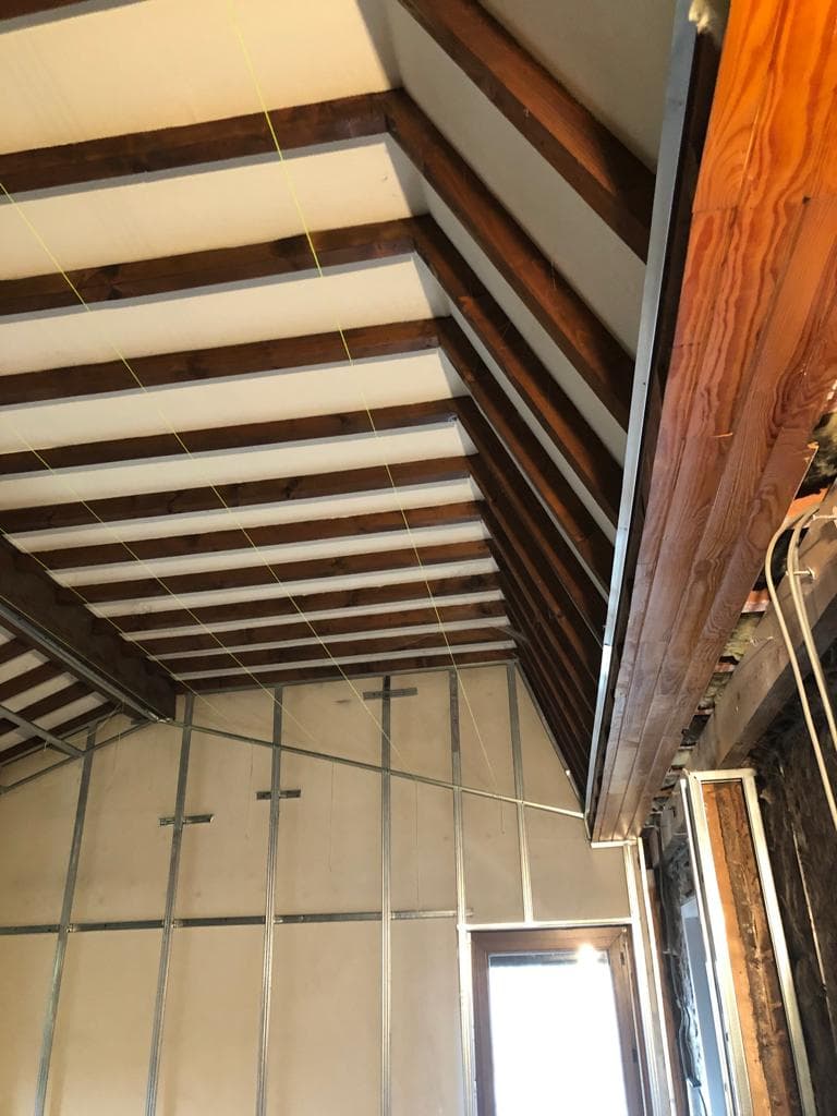Étage sous toiture en rénovation à Sallanches : chevrons bois apparents, cordeaux de traçage et ossature métallique posée sur le pignon, avant plaques de plâtre