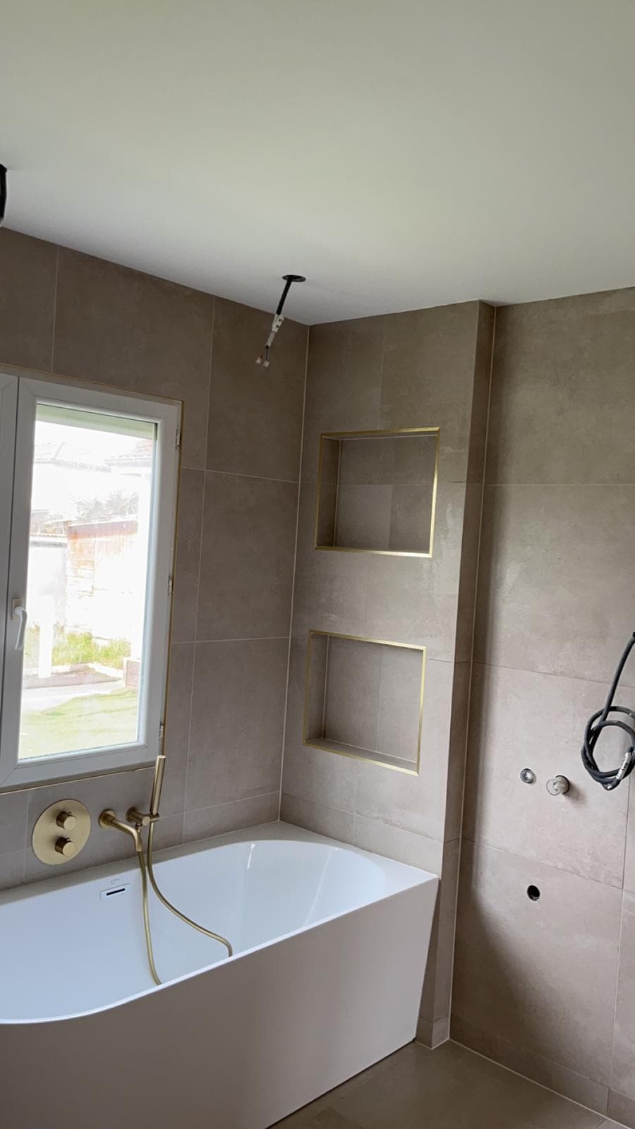 Baignoire adossée à La Motte-Servolex dans un carrelage beige grand format, deux niches superposées à profilés dorés et robinetterie or brossé