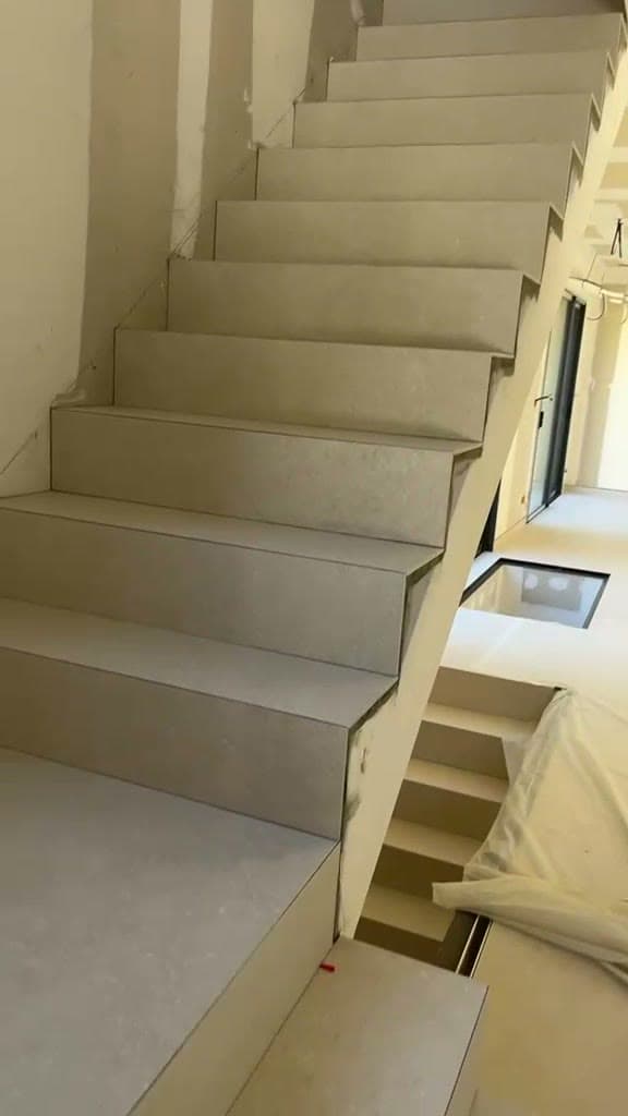 Volée d’escalier carrelée en grès cérame beige clair sur marches et contremarches, départ d’une seconde volée, murs encore bruts, à Thonon-les-Bains