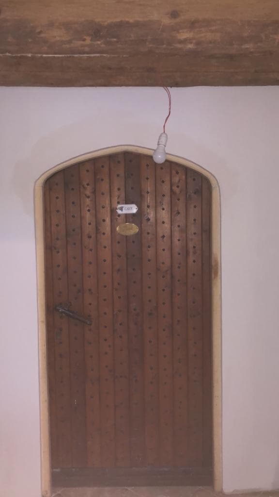 Porte de cave ancienne en bois à lames verticales cloutées dans un encadrement cintré, mur enduit blanc et poutre bois apparente
