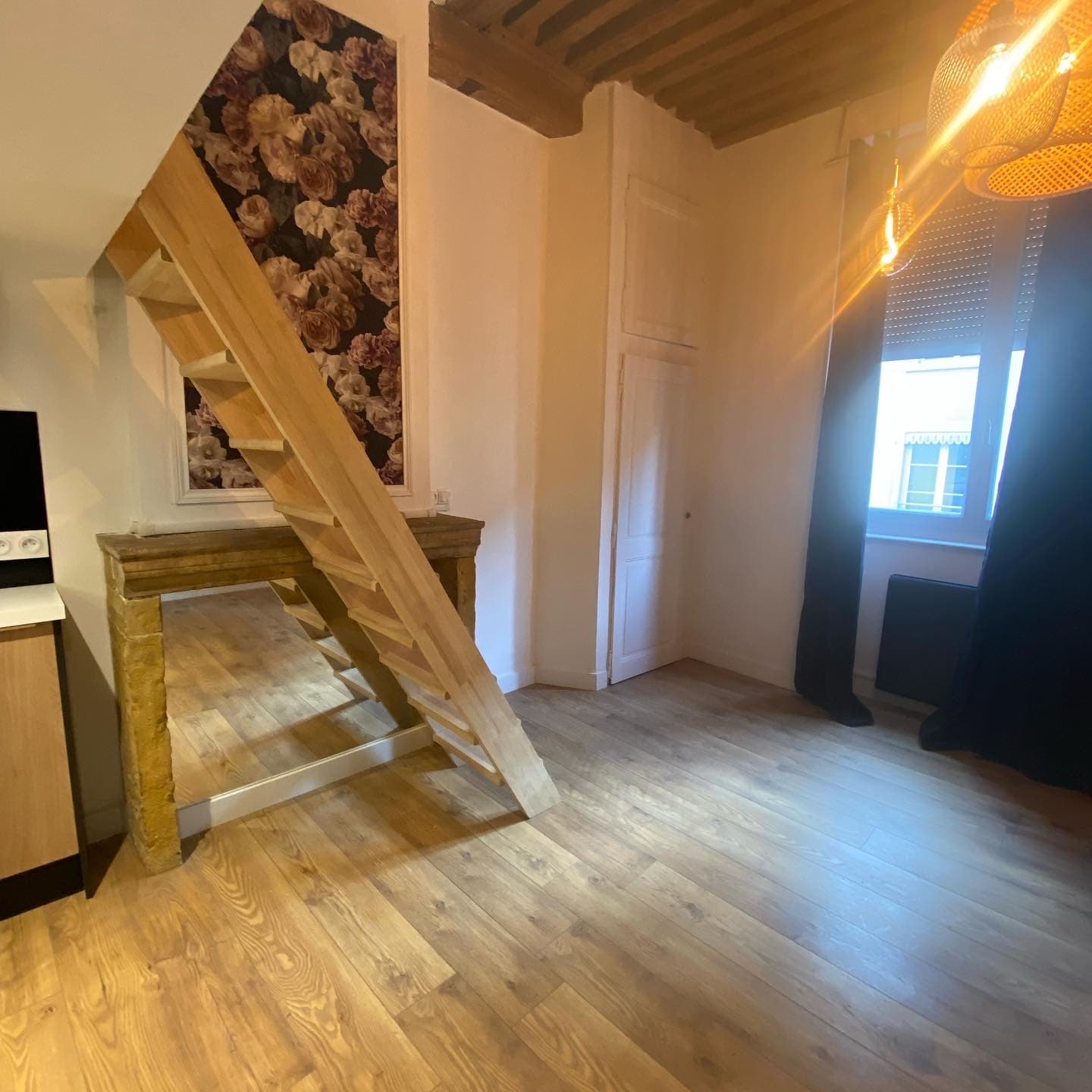 Séjour rénové à Annecy avant ameublement : échelle de meunier en bois clair, console en pierre ancienne, solives apparentes et sol aspect chêne